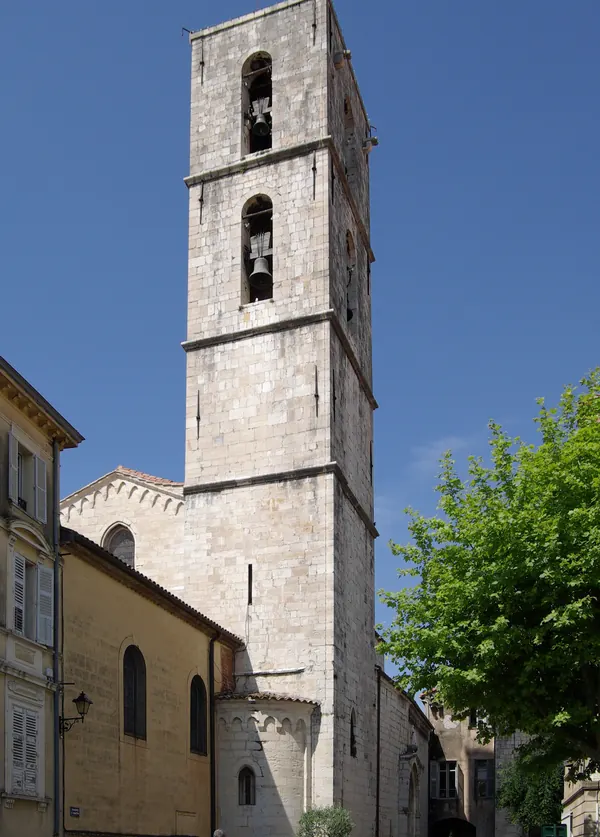 Un haut clocher de pierre dans la vieille ville de Grasse, sous un ciel bleu.