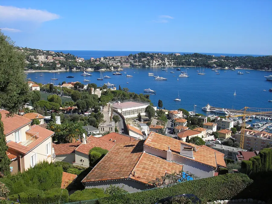 La rade de Villefranche-sur-Mer vue des hauteurs : toits de tuiles, voiliers au mouillage et le cap Ferrat au loin.