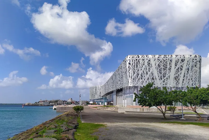 Le Mémorial ACTe et sa résille blanche au bord de l'eau, à Pointe-à-Pitre, sous un ciel de nuages.