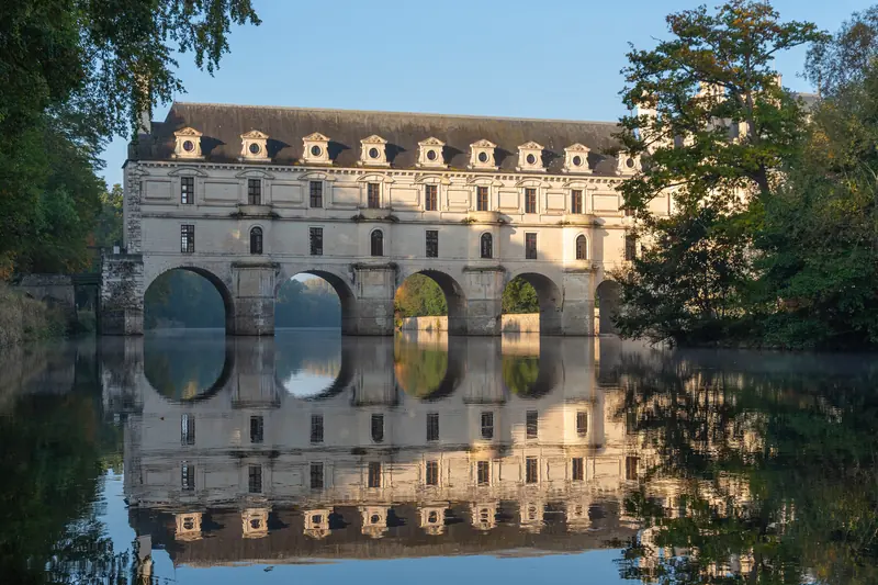 Le château de Chenonceau et ses arches au-dessus du Cher, reflétés dans l'eau calme.
