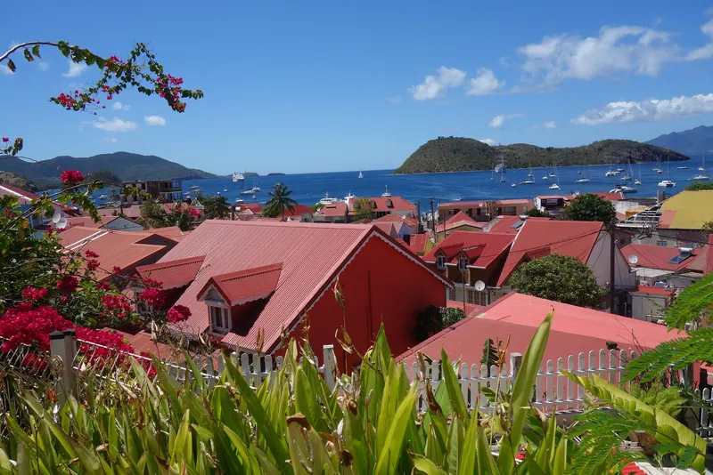 Les toits rouges de Terre-de-Haut, aux Saintes, entre les bougainvilliers, au-dessus d'une baie semée de voiliers.