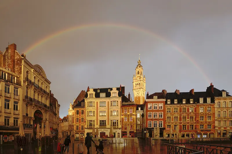 La Grand-Place de Lille et son beffroi sous un arc-en-ciel, dans la lumière du soir.