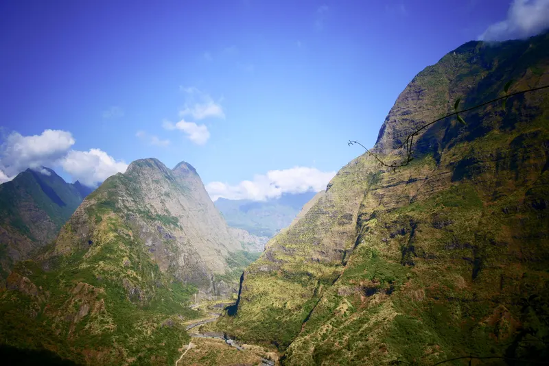 Les remparts verts du cirque de Mafate plongent vers une vallée, sous un ciel bleu.